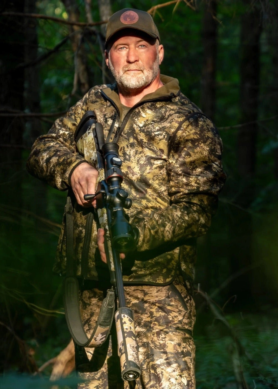 Man in camouflage clothing holding a rifle in a forest setting